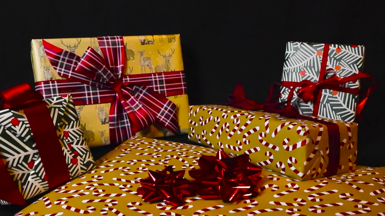 imágenes hermosas de regalos de navidad envueltos o regalos en un fondo negro oscuro mientras las imágenes se acercan a ellos. el papel de embalaje tiene bastones de caramelo, diseños festivos de vacaciones coloridos, cintas rojas visibles