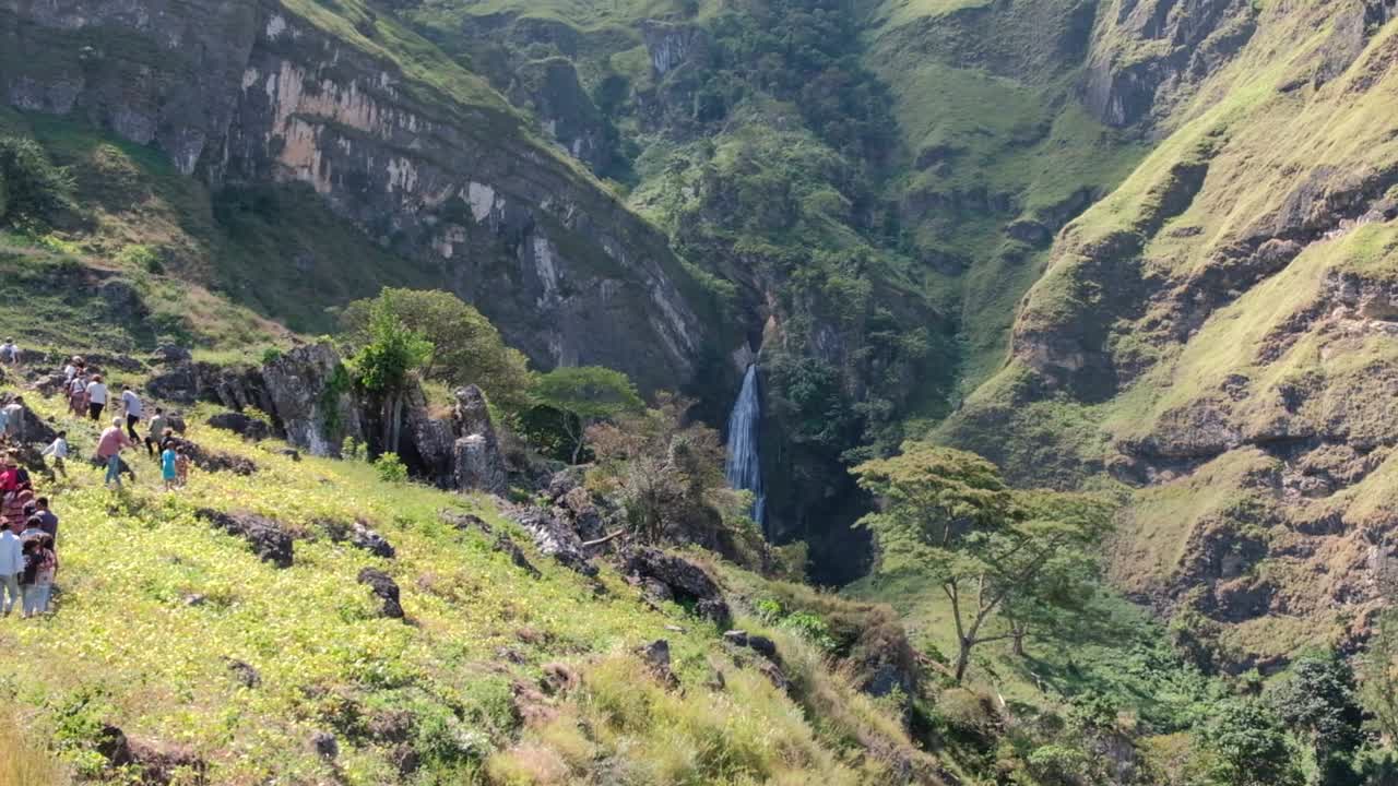 People and the local community walking to the huge Dokomali waterfall in the remote, rugged mountains of Ainaro district in rural countryside of Timor Leste, Southeast Asia
