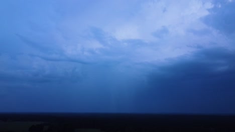 beautiful aerial view of dramatic dark thunder storm clouds in summer evening, extreme thunderstorm with several lightning strikes deep in to the clouds, distant wide angle drone shot camera tilt down