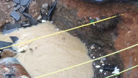 sumidero en medio de la carretera con una alcantarilla rota con agua corriendo a través de ella