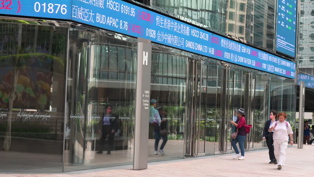 At Exchange Square, home of the Hong Kong Stock Exchange (HKEX), a moving screen displays negative stock ticker symbols as pedestrians walk through the bustling financial district of Hong Kong.