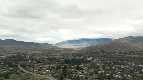 Flat-city-land-and-mountain-highland-with-a-lake-in-between-on-a-cloudy-day-in-Tafi-del-Valle,-dolly-shot-in-slow-motion-and-copy-space