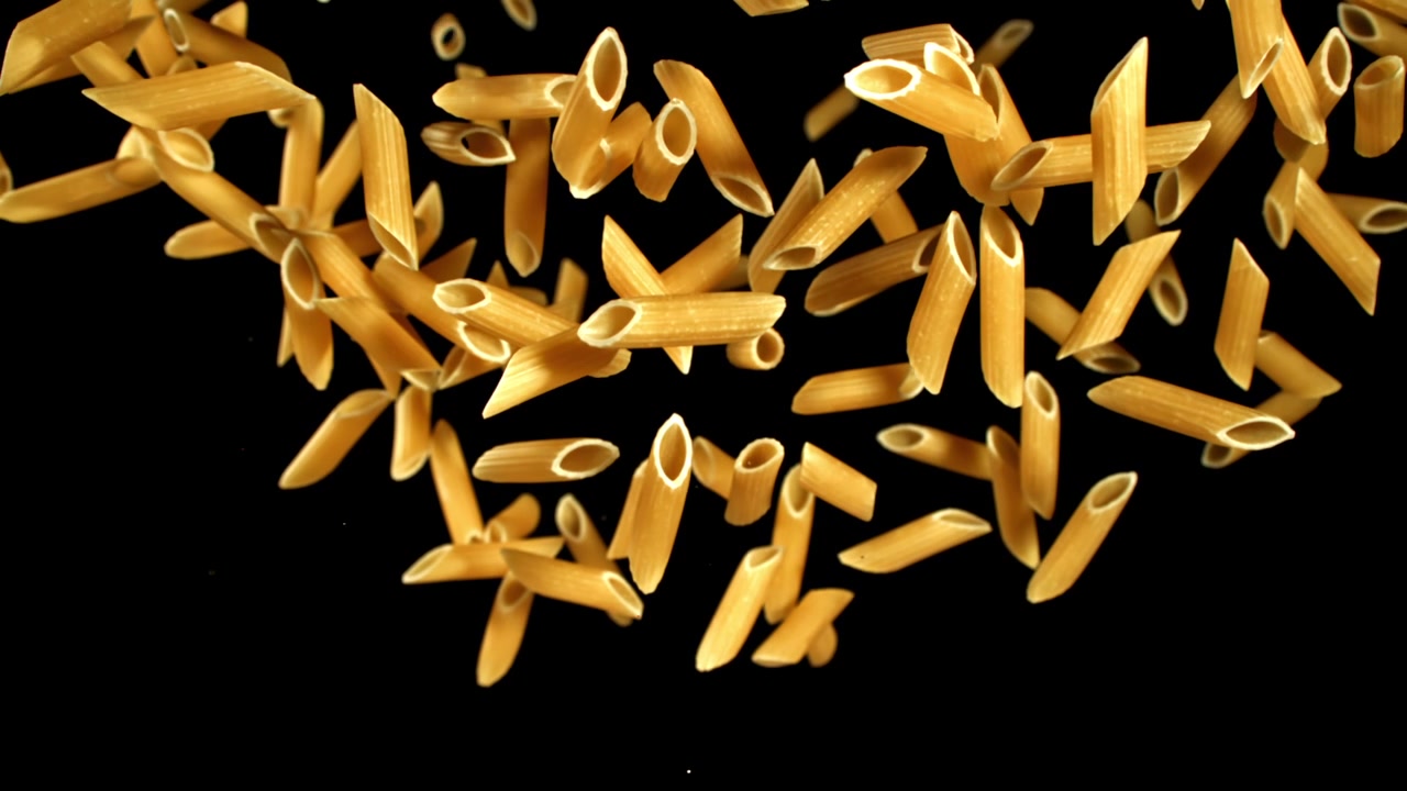 Penne secche che cadono e galleggiano al rallentatore su sfondo nero