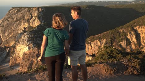 pareja romántica cogida de las manos, de pie en un acantilado rocoso