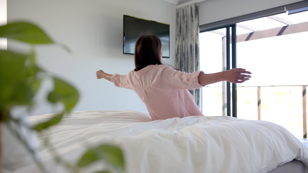 Relaxing on bed, woman watching TV in modern home bedroom