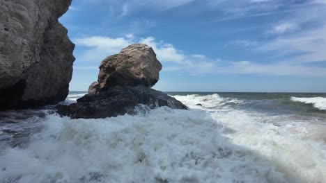 Waves-crash-against-rugged-rocks-along-the-shoreline-in-Crimea,-highlighting-the-power-of-the-Sea-of-Azov-under-a-bright-sky