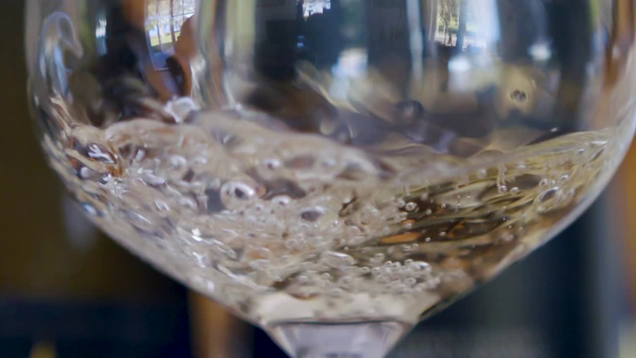 Versamento al rallentatore di vino bianco in un bicchiere che produce molte bollicine