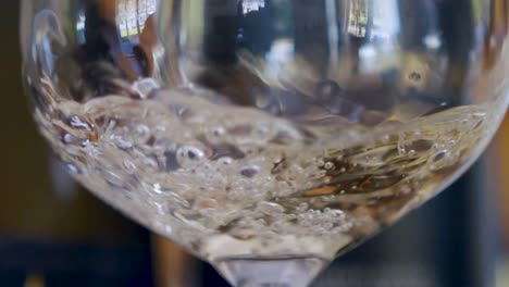 slow-motion pour of white wine into a glass producing lots of bubbles