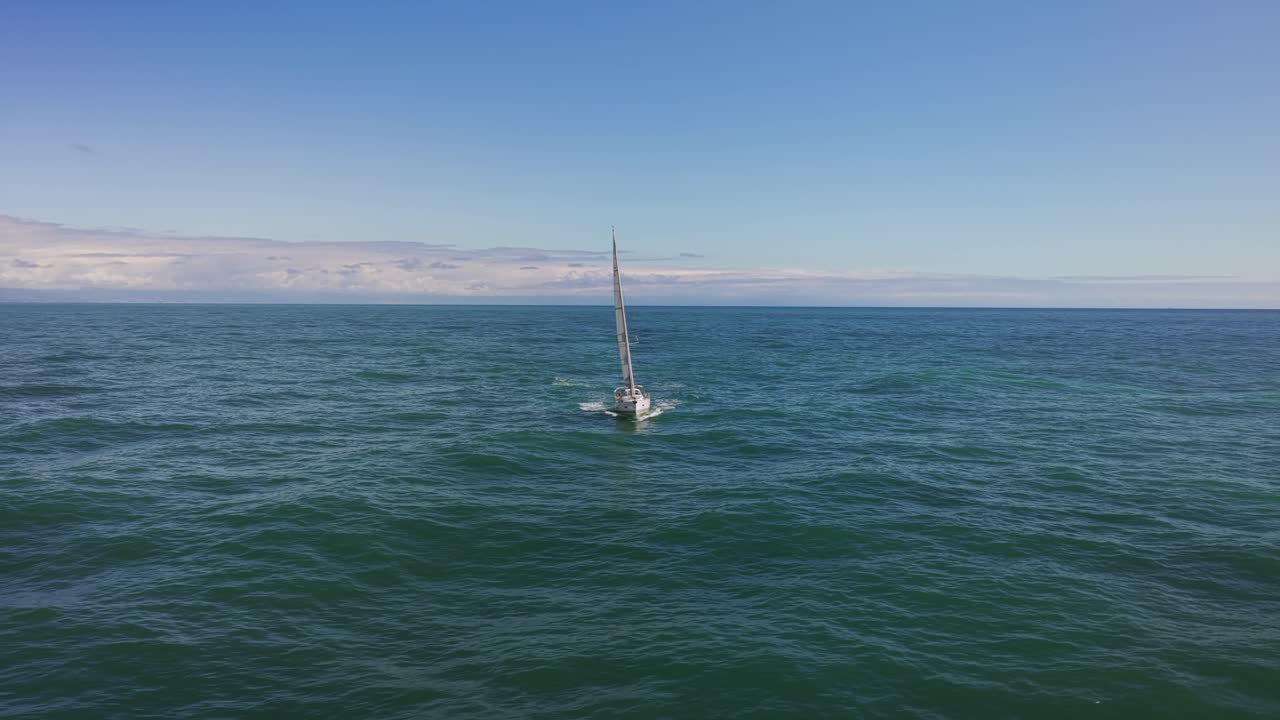 Aerial view of sailboat navigating on open turquoise sea, with Italian coast in background, Liguria. Drone orbiting at low altitude, copy space