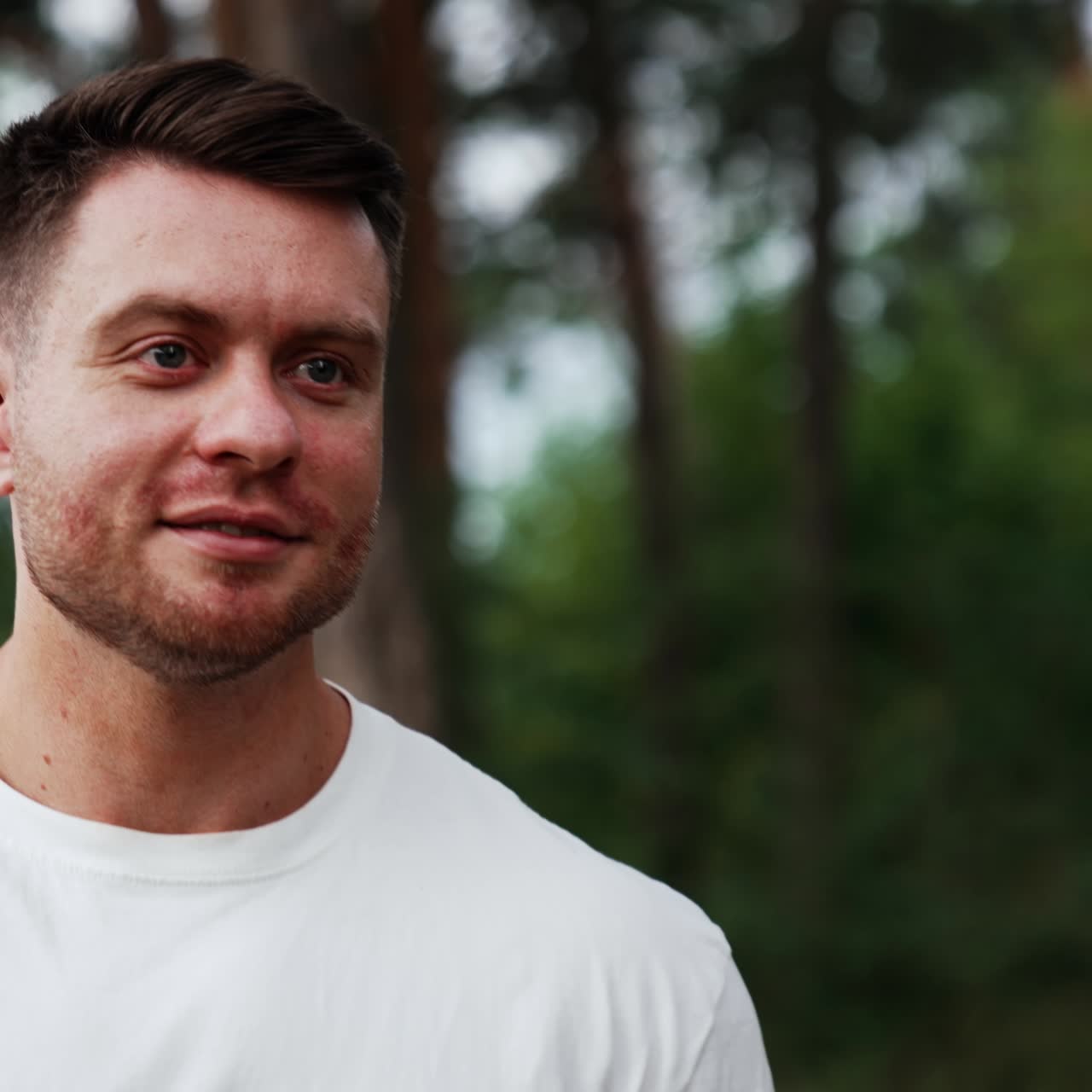 Caucasian unshaved man in white t-shirt walks in the nature. Relaxed man portrait spending time outdoors in summer