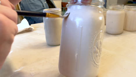 closeup of hands painting mason jars with white paint for an upcoming wedding