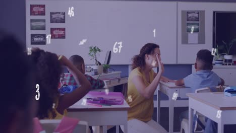 Animation-of-numbers-over-diverse-female-teacher-and-schoolboy-high-fiving-at-desk-in-class