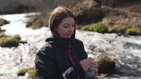 female hiker just filled her bottle with fresh water from a river coming from bruarfoss in iceland and taking a sip of it