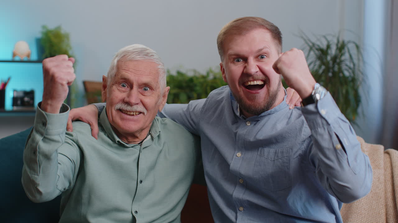 Senior grandfather with young adult man grandson shouting celebrating success winning good news