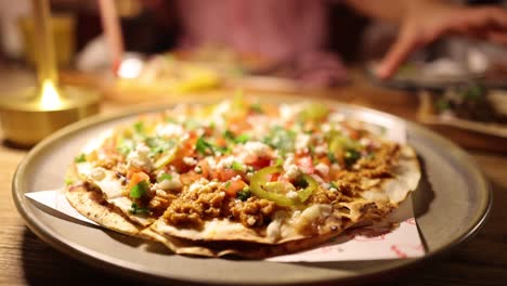 close-up of a mexican pizza on a table in a warmly lit bangkok restaurant. hands reach for food, creating a cozy dining atmosphere