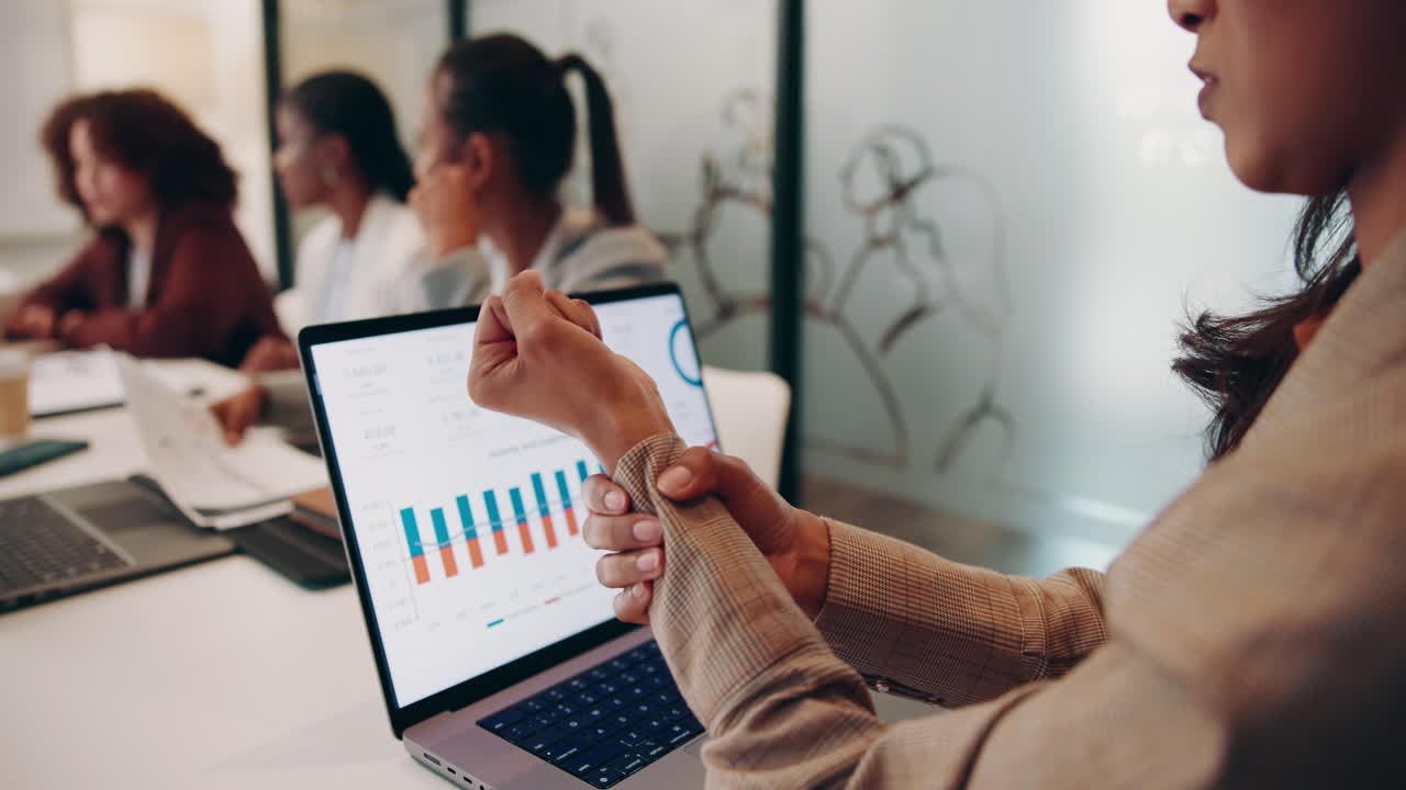A businesswoman experiencing wrist pain while looking at charts on her laptop