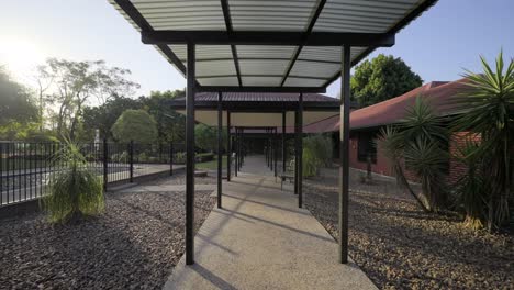 Wide-pull-back-shot-of-a-red-house-with-outdoor-breezeway,-swimming-pool-and-shone-garden