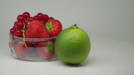 strawberries and cherries inside the white transparent bowl with lime on the outside rotating in the turntable - close up shot