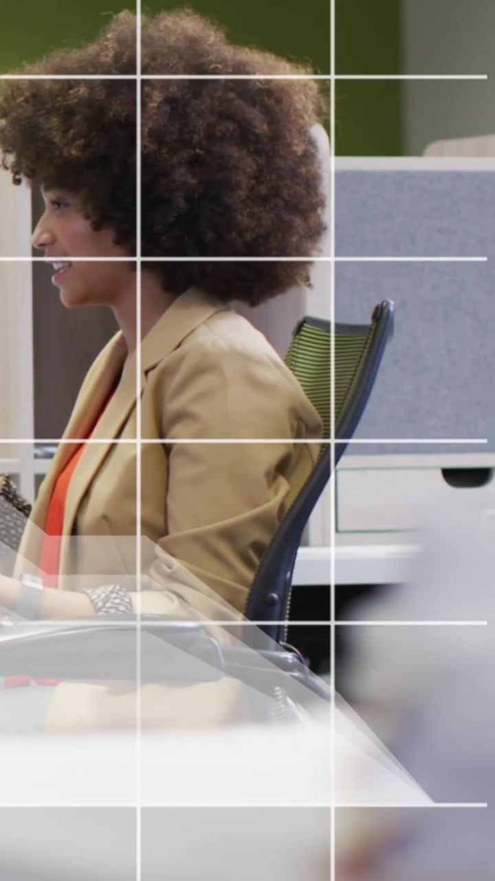 Vertical video: Woman starting work by typing at desk in office, shifting posture and smiling