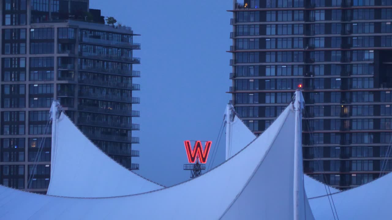 Distinctive W Neon Sign Of Woodward's Building Through Fabric Roof Of Canada Place In Vancouver, Canada