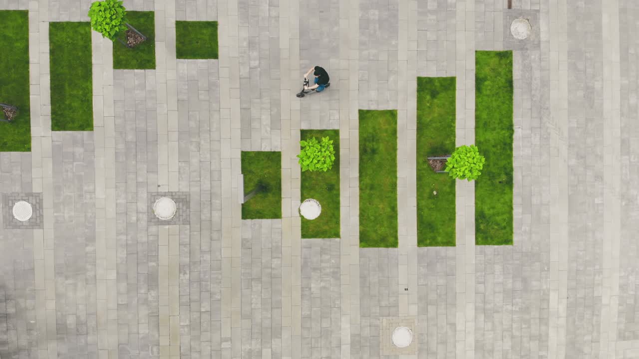 vista aérea en la parte superior joven hombre de negocios montando en el transporte del futuro scooter eléctrico sonriendo en el sol brillante entre las casas modernas.