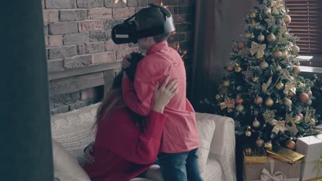 la joven madre rubia abraza a sus hijos cerca del árbol de navidad decorado.