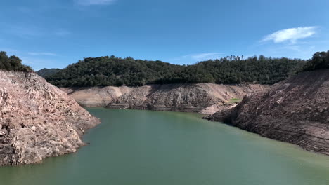 low aerial view flying between dry banks inside sau reservoir, catalonia, spain