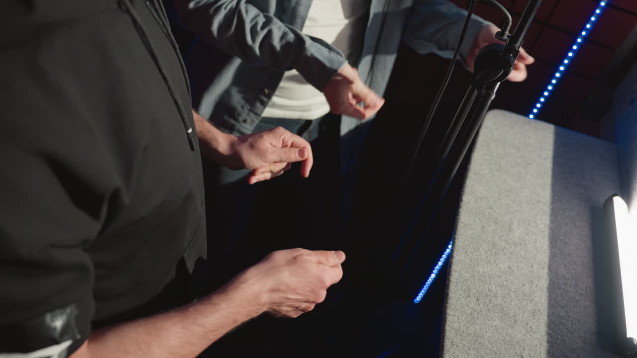 녹음 스튜디오에서 두 남자가 손가락을 리하게 는 클로즈업, 그들의 손과 캐주얼 의상에 초점을 맞추고, 스튜디오 장비와 녹색 led 조명과 함께 창의적인 분위기