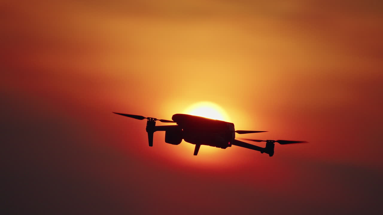 Drone flyver foran den glødende sol under solnedgang med dramatisk orange himmel