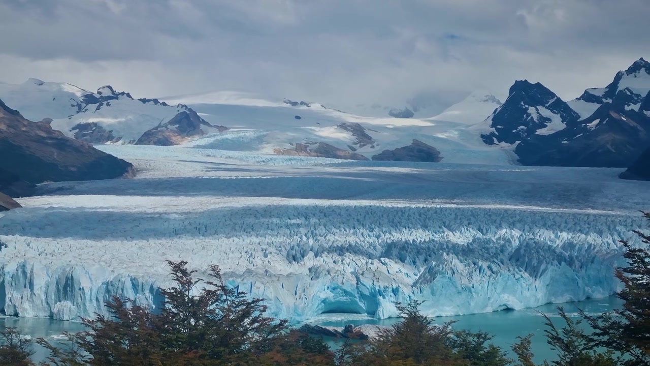 L'immenso Ghiacciaio Perito Moreno domina l'aspro paesaggio patagonico, il suo vivido ghiaccio blu contrasta con imponenti montagne e una natura incontaminata sotto un cielo nuvoloso in Argentina