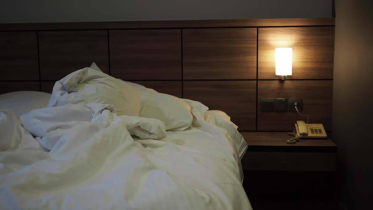 Ranjang yang Belum Dirapikan dengan Seprai Putih dan Bantal di Kamar Hotel