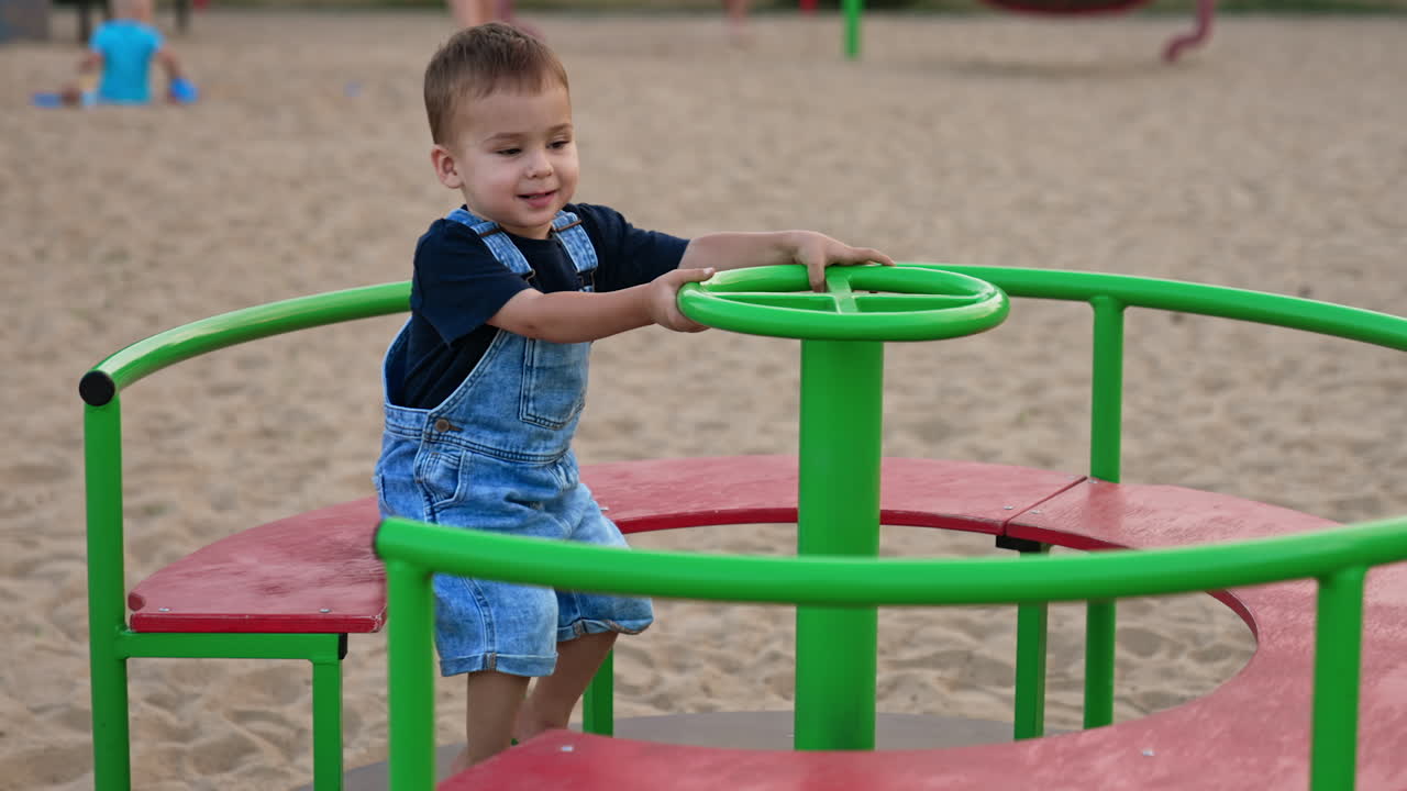 Adorable cute baby sitting on a merry go round. Little Caucasian child spending time on the playground in summer.