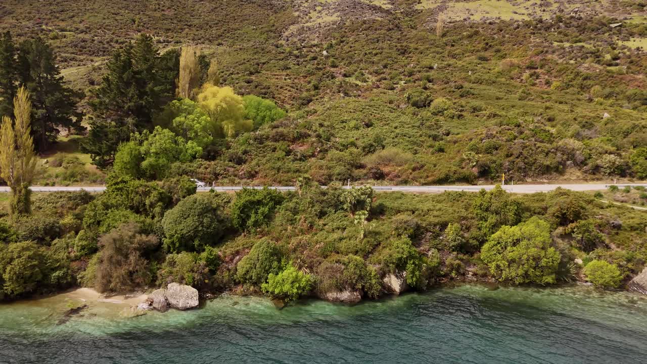 Ripresa aerea scorrevole di un furgone turistico che percorre il Lago Wakatipu nella regione di Otago, sull'Isola del Sud della Nuova Zelanda, circondato da colline boscose sempreverdi