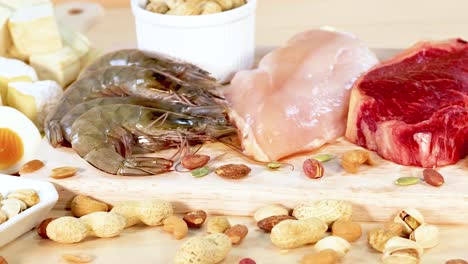 una variedad de alimentos ricos en proteínas, incluidos nueces, huevos, mariscos y carnes, están artísticamente dispuestos en una superficie de madera