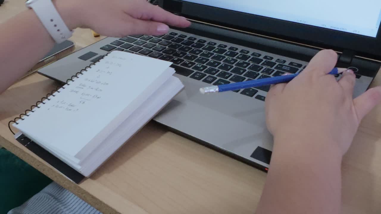 Modern desk setup for work: hands writing notes, laptop, coffee, and smartwatch.