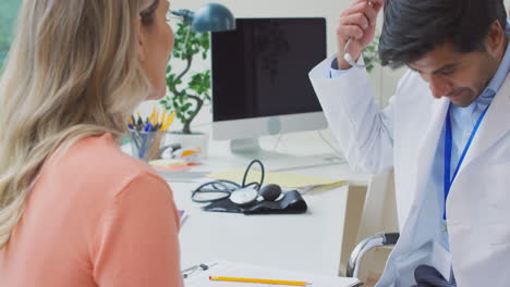 male doctor or gp examining mature female patient listening to heartbeat with stethoscope