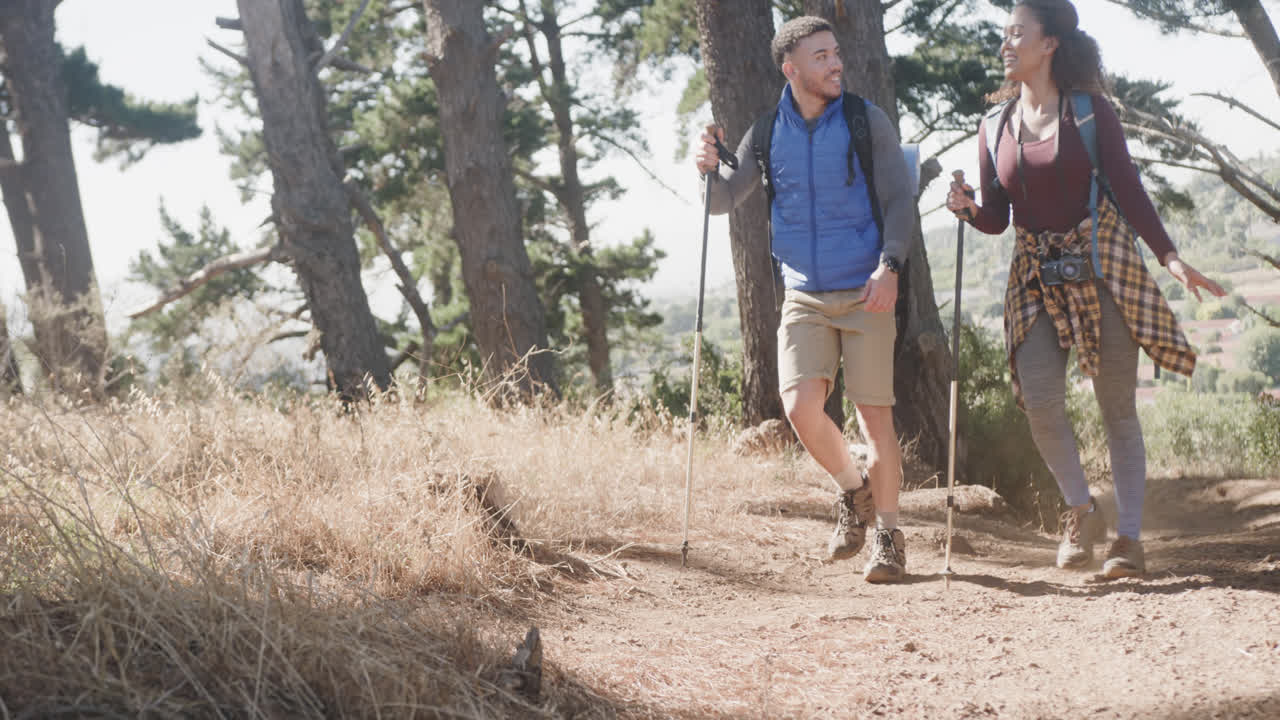 Felice coppia afroamericana che fa escursioni con bastoncini da trekking nella foresta, al rallentatore