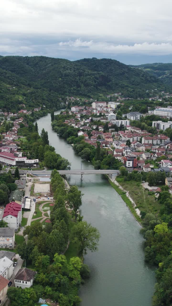 Pemandangan udara Sungai Vrbas melintasi kota Banja Luka di Bosnia dan Herzegovina, menampilkan jembatan dan bangunan di sepanjang tepi sungai. Video Vertikal