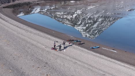 adventure kayakers resting on shore pebble beach in iceland, reflection of hólmatindur mountain on water