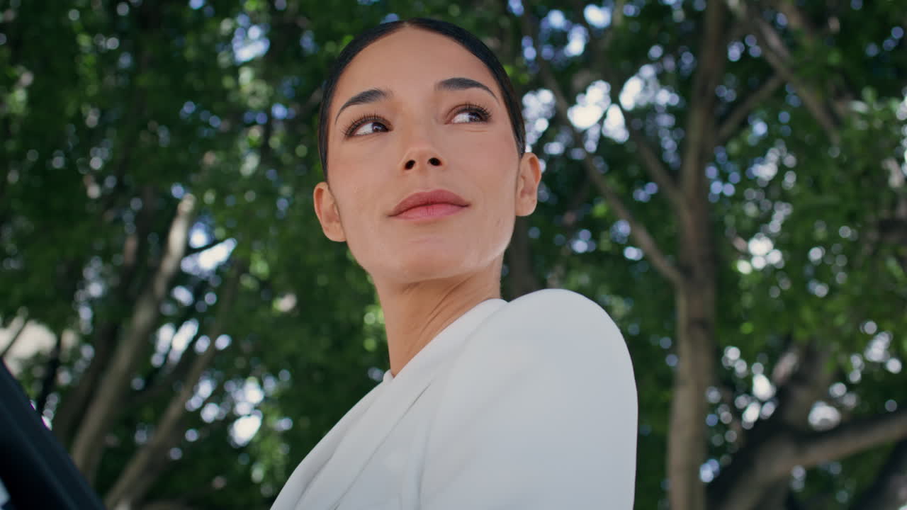 부유한 사업가 여성이 녹색 공원 근접에서 서서 둘러보고 있습니다. 고급스러운 여성이 포즈를 취하고 있습니다.