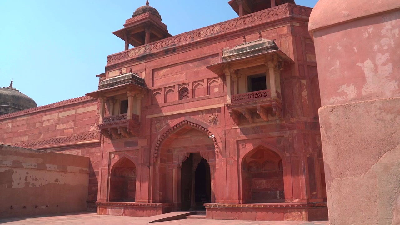 Hindistan'ın Uttar Pradesh eyaletindeki Fatehpur Sikri'de bulunan Jodha Bai Sarayı'nın süslü kırmızı kumtaşı girişi ve jharokha balkonlarına doğru yavaşça yakınlaşan çekim.
