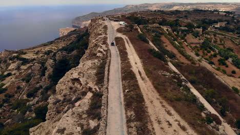 Quad-De-Seguimiento-Aéreo-En-Camino-De-Tierra-Cerca-Del-Borde-Del-Acantilado,-Telón-De-Fondo-Marino