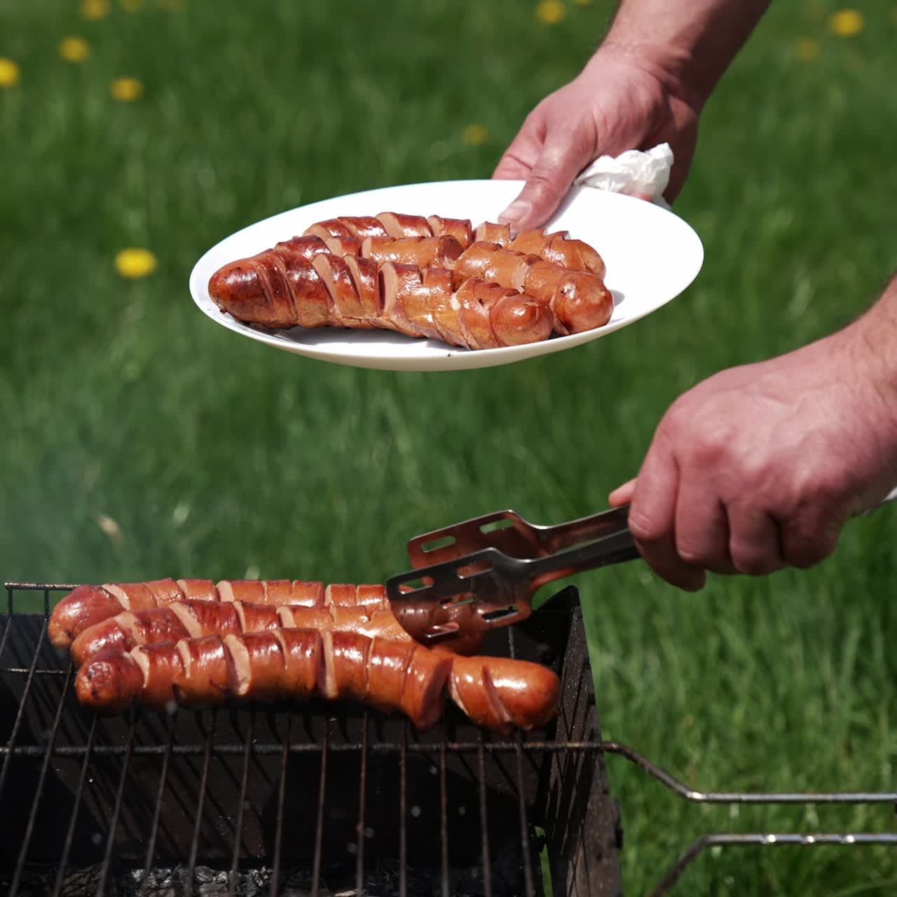 Chef taking off ready sausages from a grill. Man putting delicious roasted hot dog sausages on a plate with a tongs. Barbecue for outdoor lunch