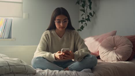 Caucasian-teenage-girl-browsing-phone-while-sitting-on-bed-in-her-bedroom