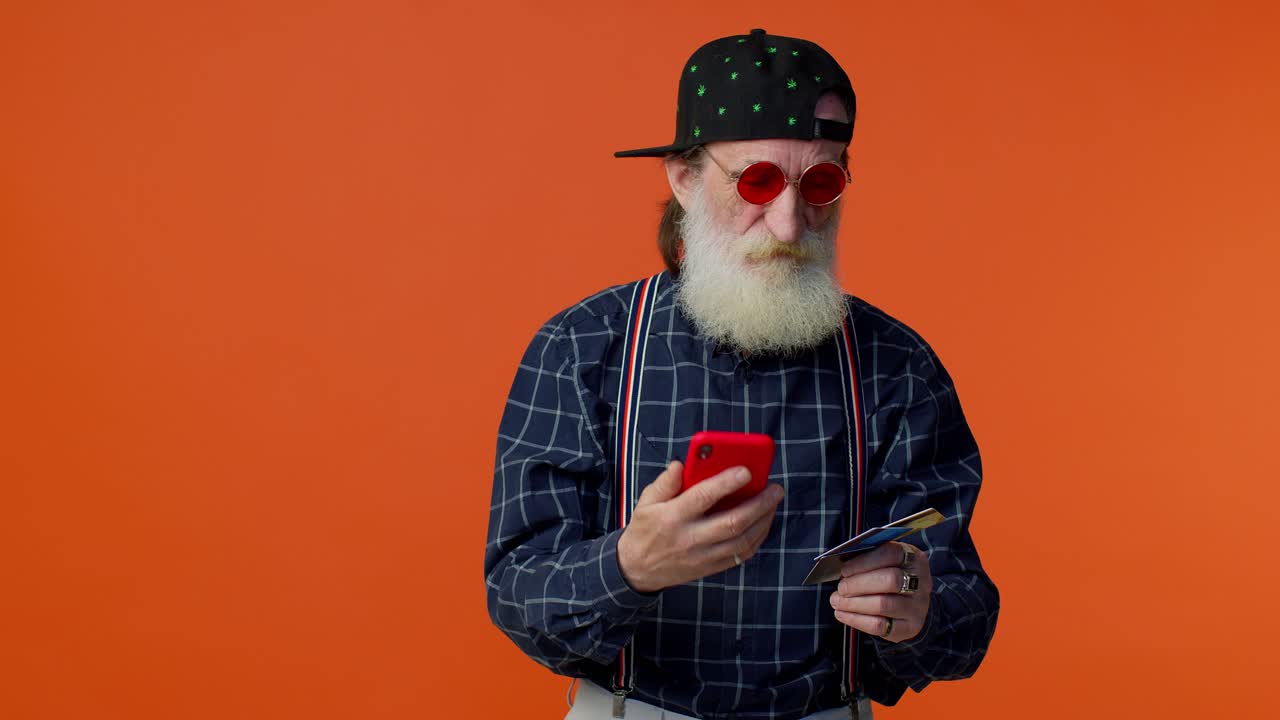 Ældre, stilfuld skægget mand bruger kreditkort og smartphone til online shopping.
