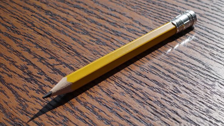 Close-up, angled shot of a yellow pencil on a wooden surface, highlighting texture and light