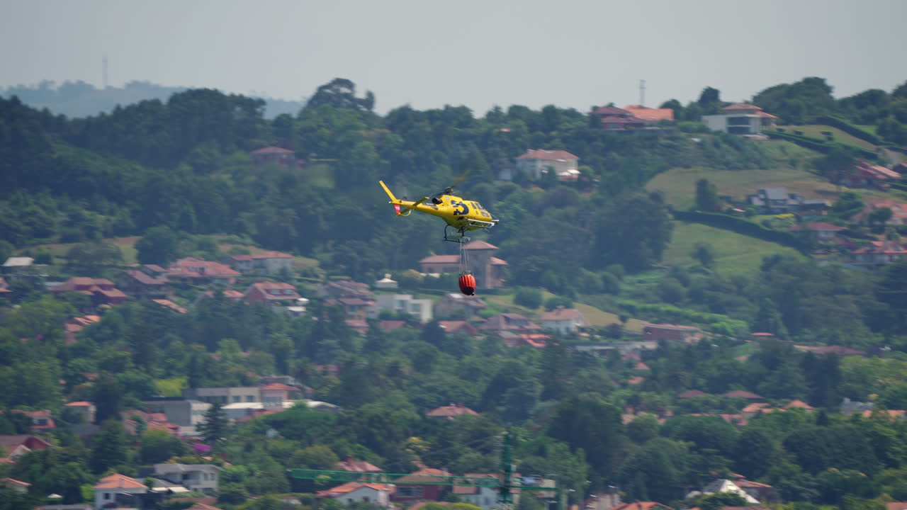 Yellow firefighting helicopter flying in the sky with a red Bambi Bucket attached for aerial water drop
