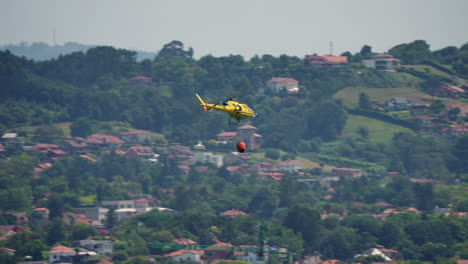 yellow firefighting helicopter flying in the sky with a red bambi bucket attached for aerial water drop