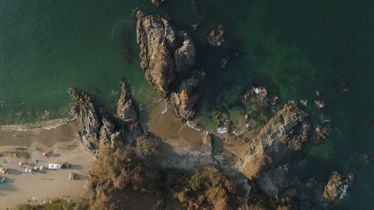 Ripresa aerea in discesa verso una piccola insenatura rocciosa mentre le onde si infrangono su una bellissima spiaggia, 4K