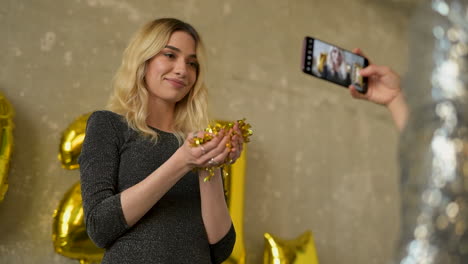 young pretty woman blowing gold glitter confetti and wearing evening dress on new year's eve